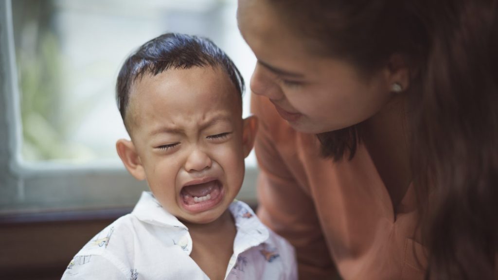 Asian mother comforts her crying son. Focus is on boy.