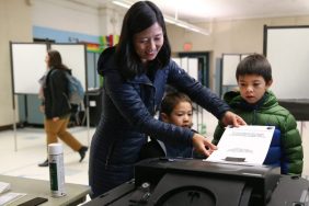 Boston Mayor Michelle Wu places her ballot into the machine at the Bates School, as her two sons looked on.