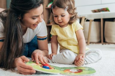 Young beautiful mother reading book with toddler daughter on the floor at home