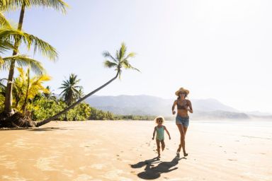 A mother and her daughter running down a palm tree scattered beach in Costa Rica.