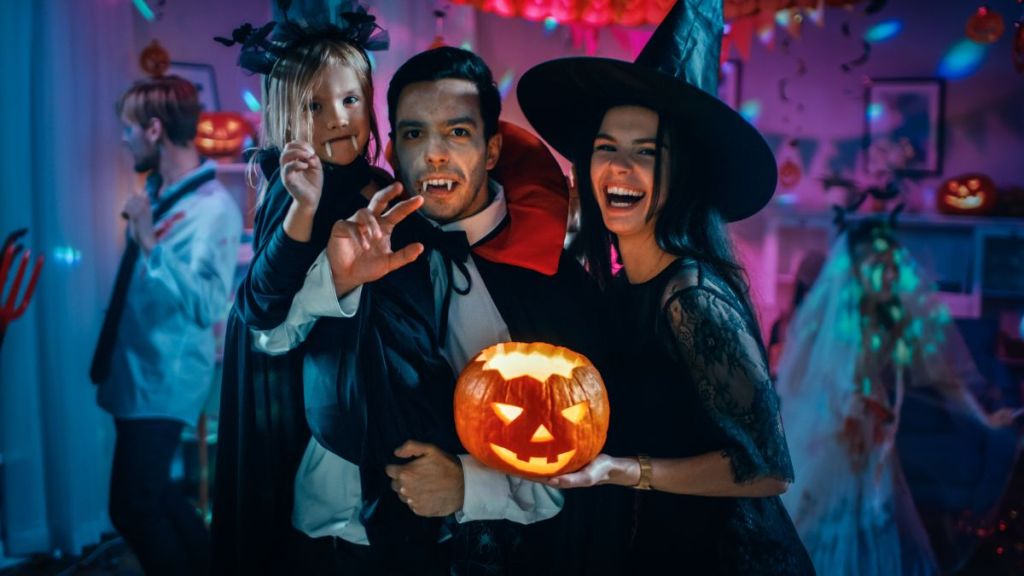 Halloween Costume Party: Dad Count Dracula Holds Little Bat Kid Daughter and Hugs Witch Mom for a Happy Family Portrait.