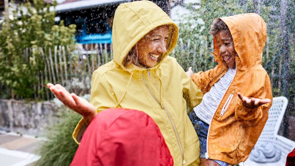 Happy mother with son in rainy garden wearing raincoats