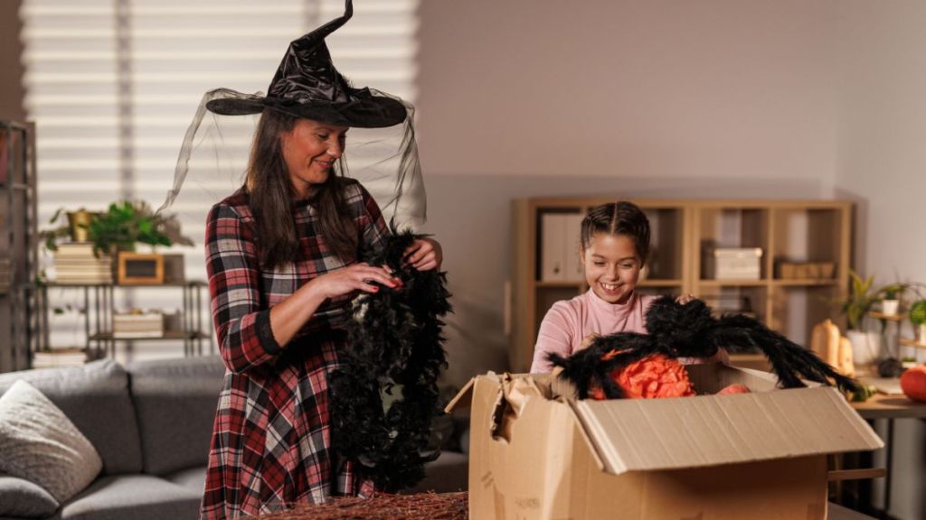 Candid shot of mid adult woman and her daughter discovering Halloween decorations that they are unpacking from a cardboard box before decorating their home.