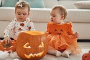 Twin sisters on Halloween day. They are indoors with a pumpkins, playing around.