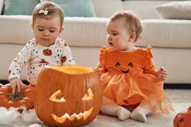 Twin sisters on Halloween day. They are indoors with a pumpkins, playing around.