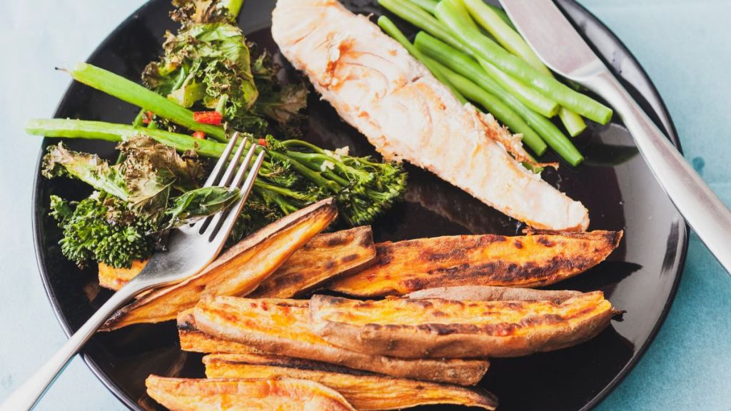 Overhead view of sweet potato wedges and salmon fillet served with tenderstem broccoli and green beans that make for a delicious sheet pan Thanksgiving recipe.