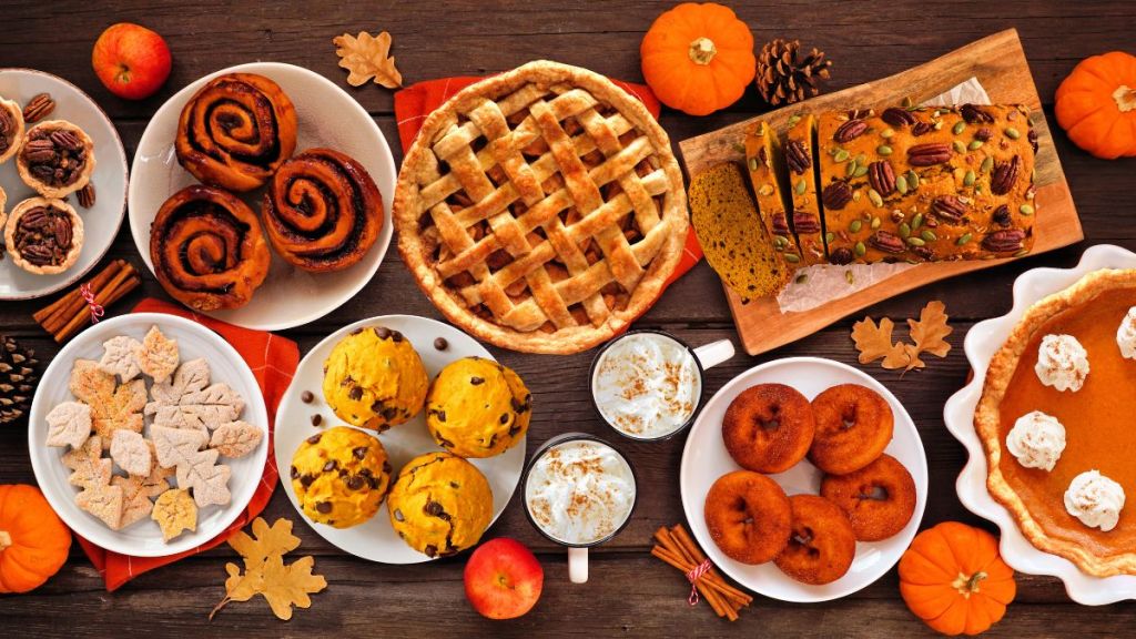 Autumn desserts table scene with a selection of traditional fall sweet treats. Overhead view over a rustic wood background. Pumpkin and apple pies, apple cider donuts, muffins, cookies, tarts.