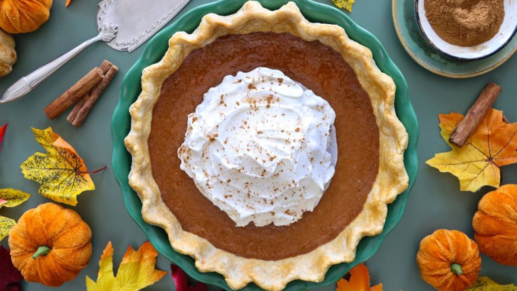 Stock photo showing close-up, elevated view of a tart tin case lined with freeform fluted, pastry that has been filled with a pumpkin puree to make a freshly baked pumpkin pie. Home baking concept.