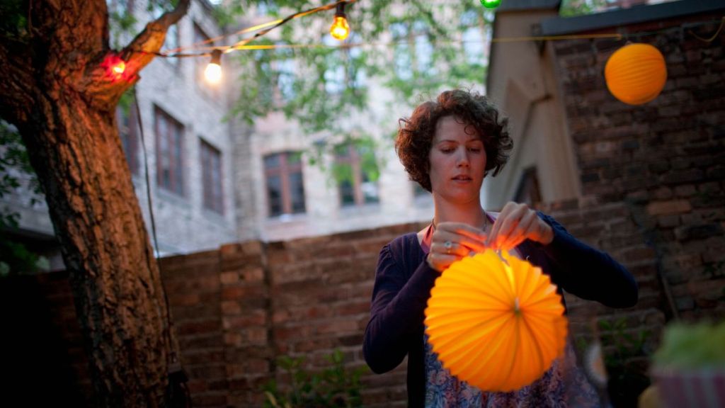 Young woman preparing paper lantern in back yard for garden party