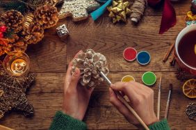 Individual doing DIY using pinecone while surrounded by craft materials and other quintessential fall items.