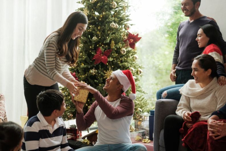 A happy family sitting next to the christmas tree and giving presents to each other.