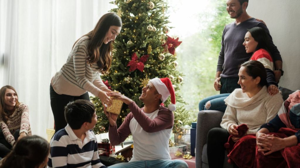 A happy family sitting next to the christmas tree and giving presents to each other.