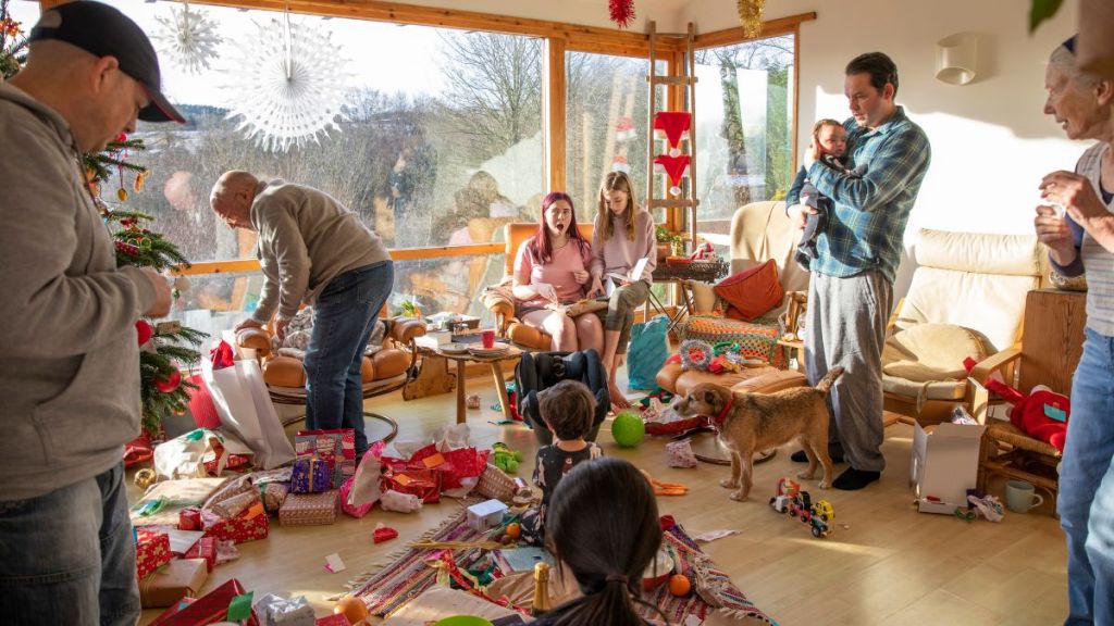 A shot of a family sitting with their Christmas gifts on Christmas Day, they are sitting together around the living room which is decorated in Christmas Decorations.