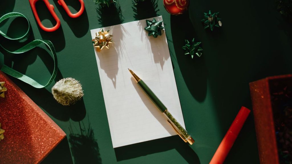 Blue notebook with a sheet of paper in female hand on green background to writing a to-do list and goals and . Christmas tree and New Year concept