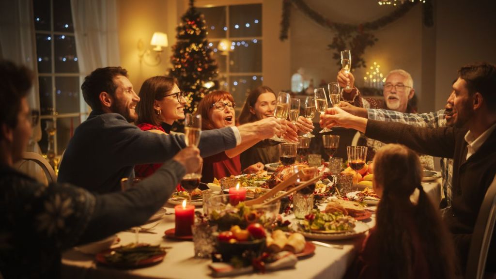 Portrait of a Handsome Young Black Man Proposing a Toast at a Christmas Dinner Table. Family and Friends Sharing Meals, Raising Glasses with Champagne, Toasting, Celebrating a Winter Holiday