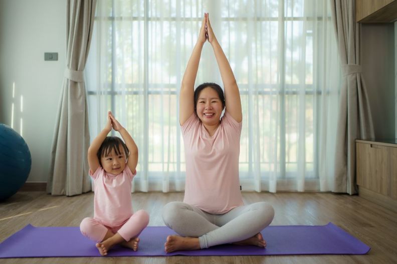 Asian young pregnant mother practicing yoga with daughter in living room at home.