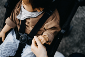 Mother holding baby girl's tiny hand who is sitting on stroller in park