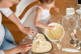 Top view of mother and little daughter making a cake together in kitchen at home for Valentine's Day.