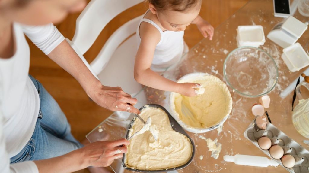 Top view of mother and little daughter making a cake together in kitchen at home for Valentine's Day.