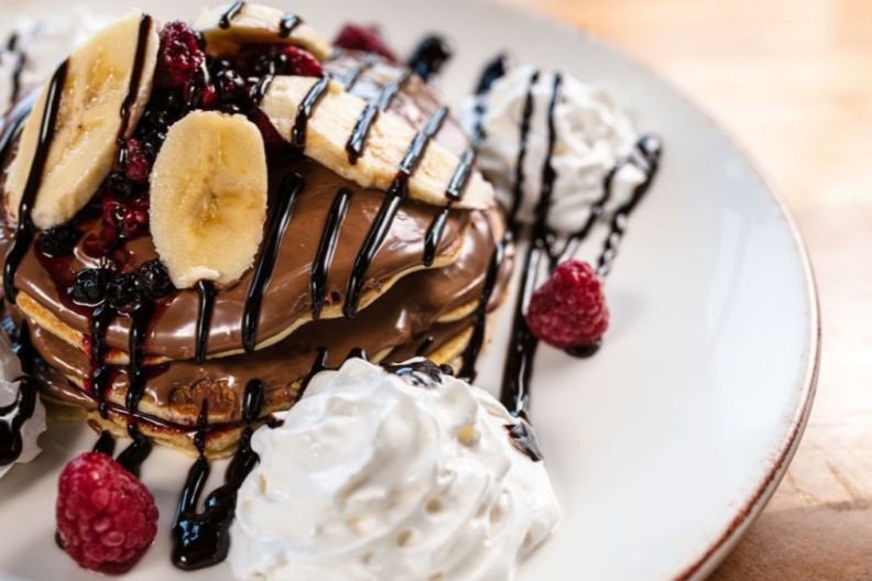 Delicious gluten-free pancakes topped with chocolate sauce, banana slices and raspberries, perfect breakfast recipe for Valentine's Day.