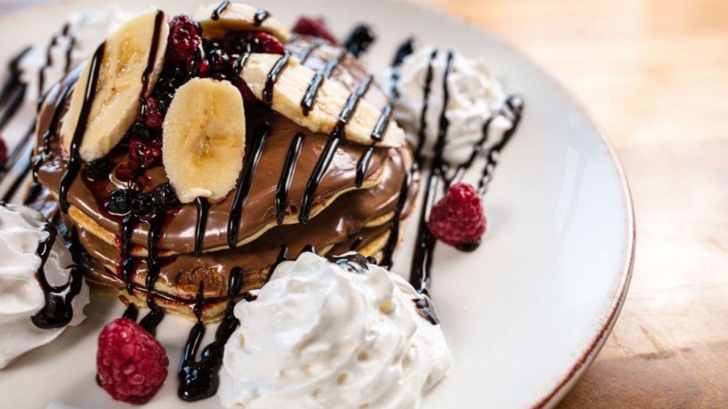 Delicious gluten-free pancakes topped with chocolate sauce, banana slices and raspberries, perfect breakfast recipe for Valentine's Day.