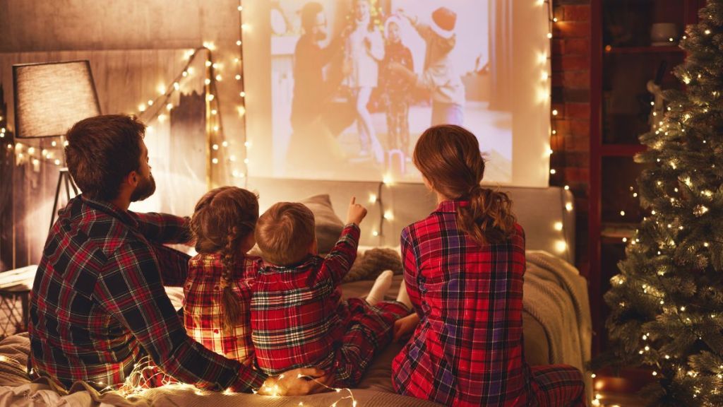 Happy family in checkered pajamas: mother father and children watching projector, film, movies with popcorn in Valentine's Day evening at home.