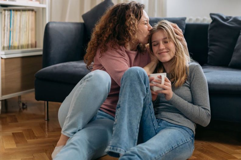 mother kiss her daughter while sitting on floor in living room