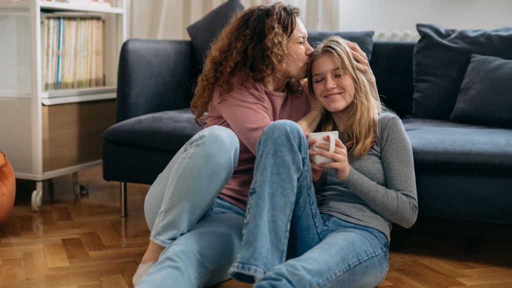 mother kiss her daughter while sitting on floor in living room