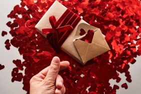 Craft gift and envelope with many red shiny hearts. Hand with thumb and index finger shows heart symbol in asia. A wonderful photo for Valentine's Day.